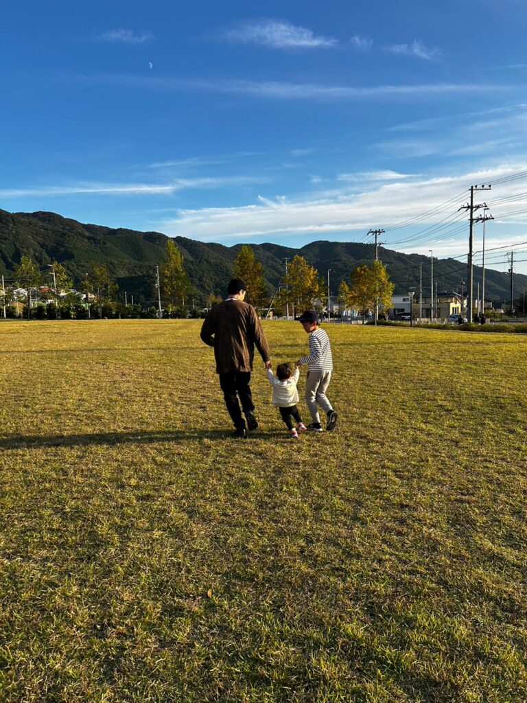 家族と手を繋いで芝生の上を歩いている画像